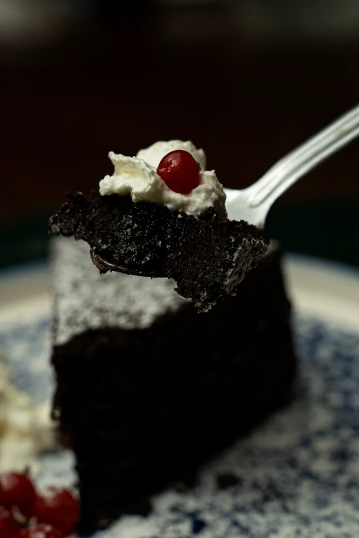 Una fetta di torta al cioccolato con panna e ribes sulla forchetta – La Vecchia Rama, Negrar